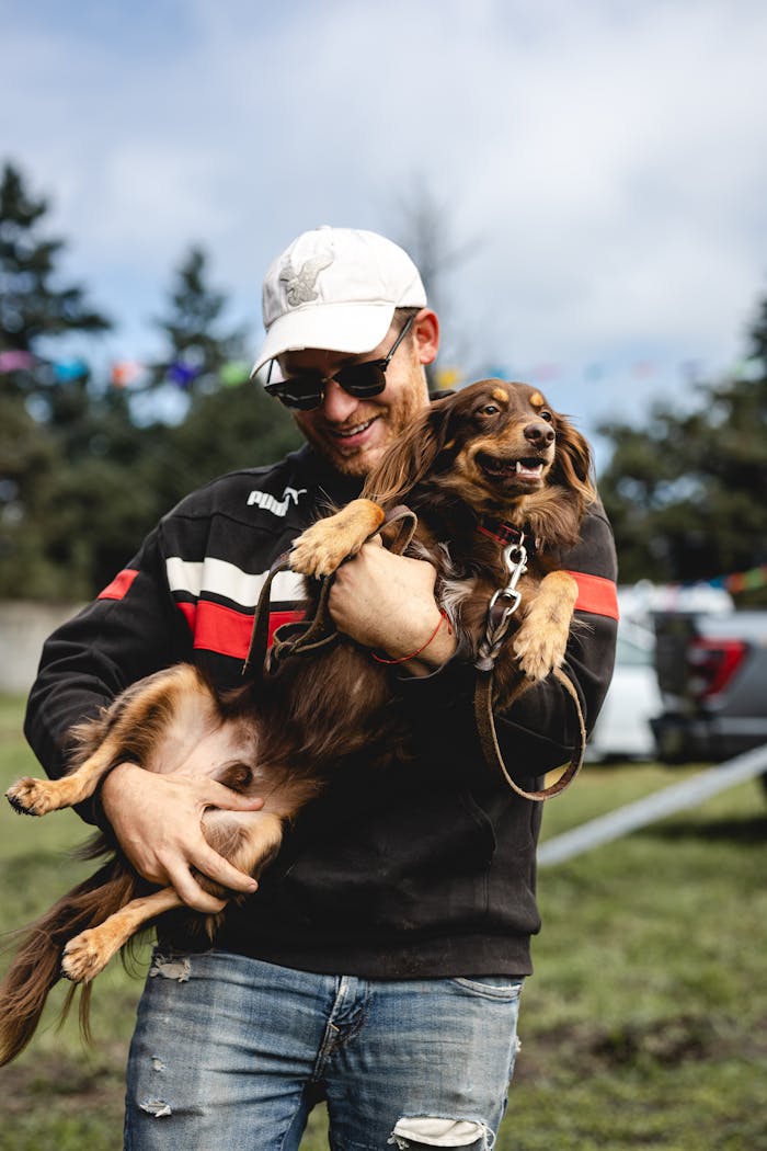 Smiling man in casual attire joyfully holds his cheerful dog outdoors.